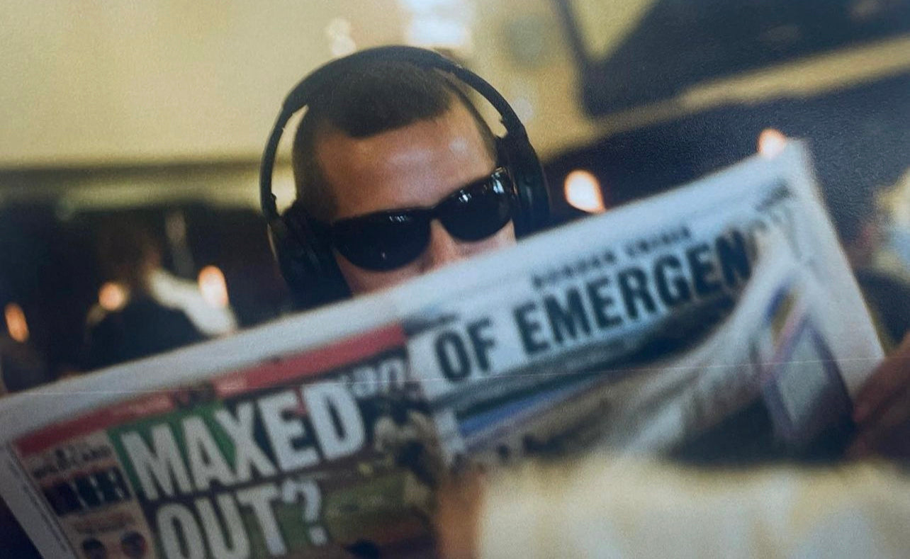 man reading a newspaper. he is wearing sunglasses and headphones.