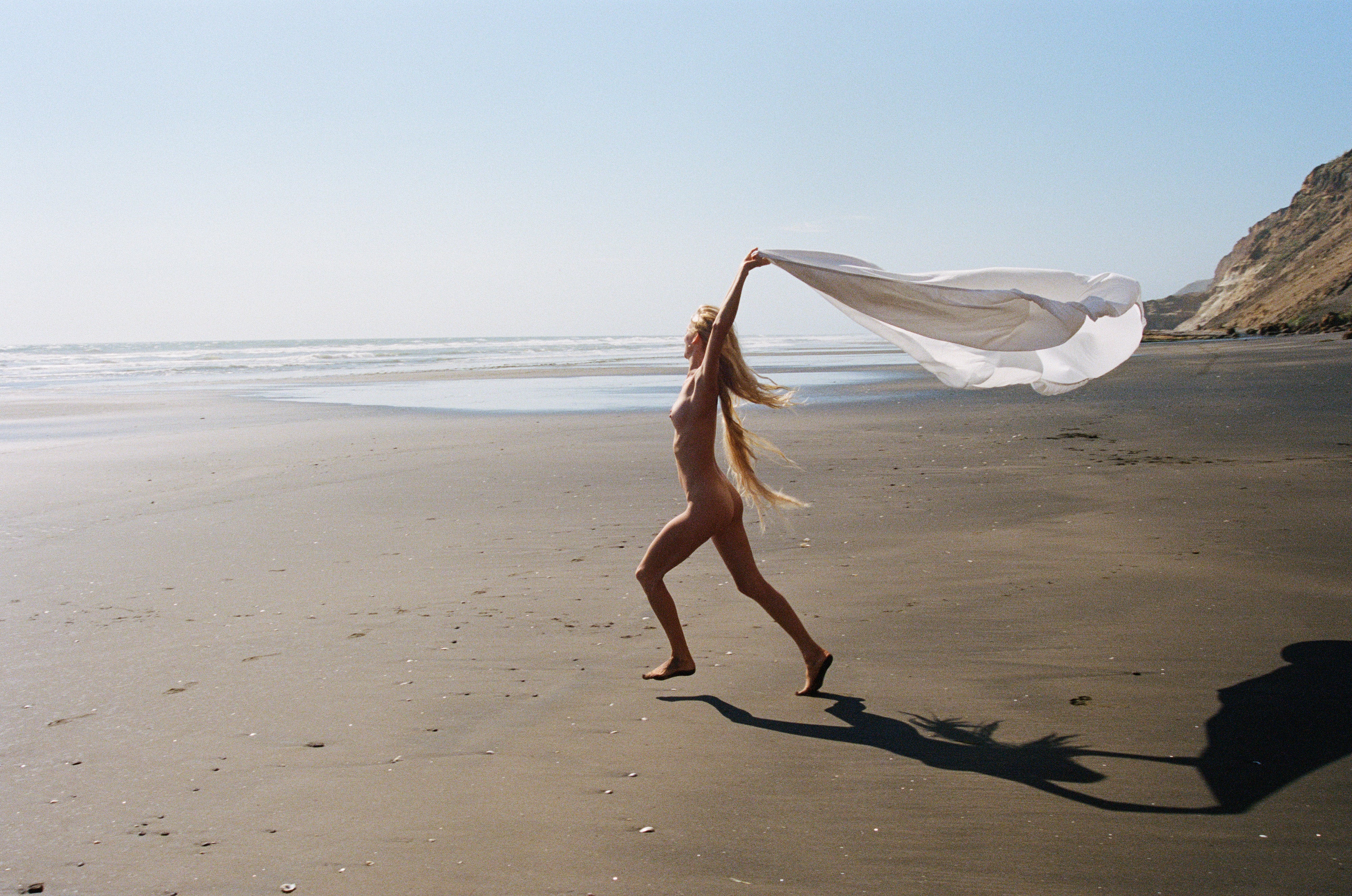 woman running on a beach holding a beach towel up in the air