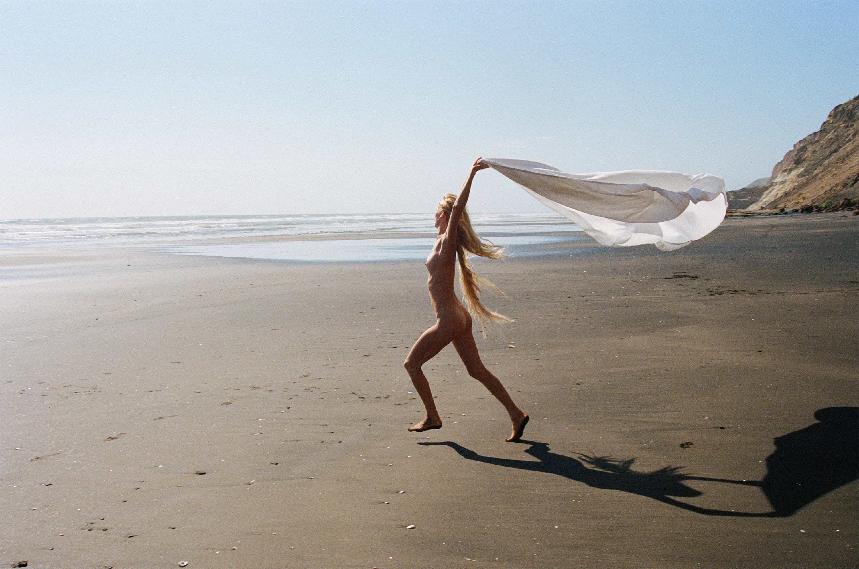 woman running on a beach holding a beach towel up in the air